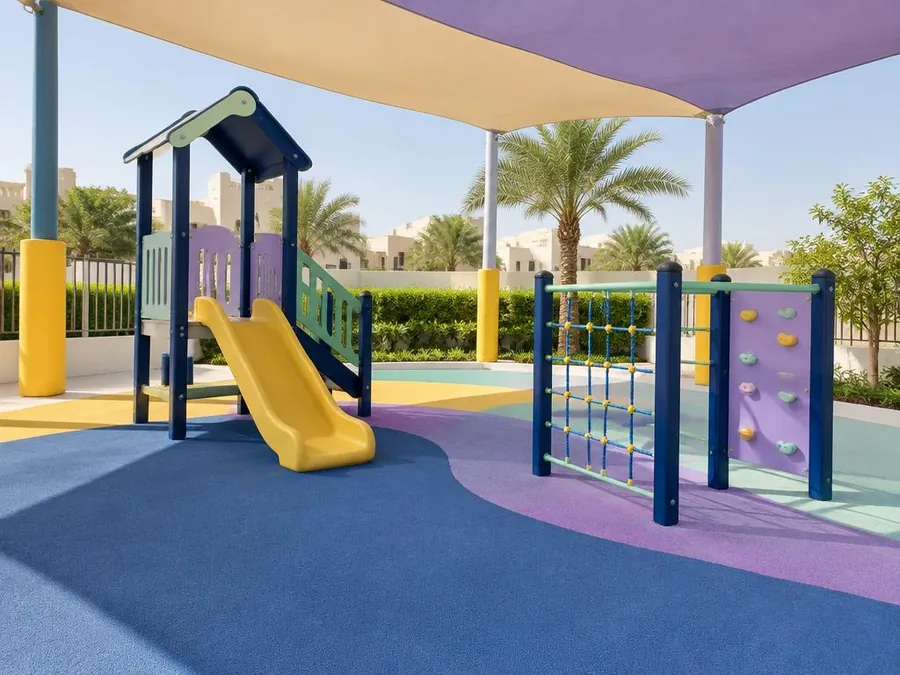 Shaded outdoor playground with a small slide and climbing frame on soft safety flooring