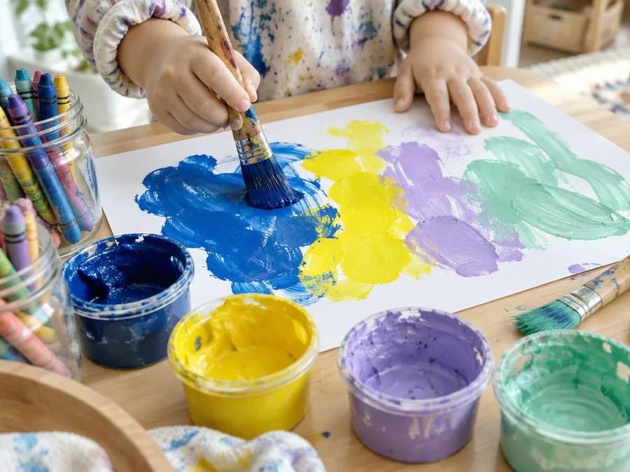 A young child's hands painting with a chunky brush in indigo, yellow, lilac and mint